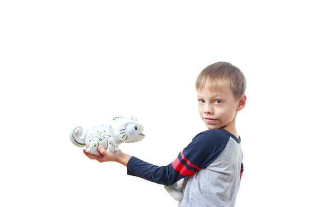 Ερωτοχτυπημένο παιδί που παίζει πλαστικό παιχνίδι-σαύρα ρομπότ με τηλεχειριστήριο, απομονωμένο σε λευκό φόντο. Το νανο-παιχνίδι Chameleon έφτυσε μια γλώσσα στο παιδί. Σύγχρονη τεχνολογία παιχνιδιών. - Φωτογραφία, εικόνα