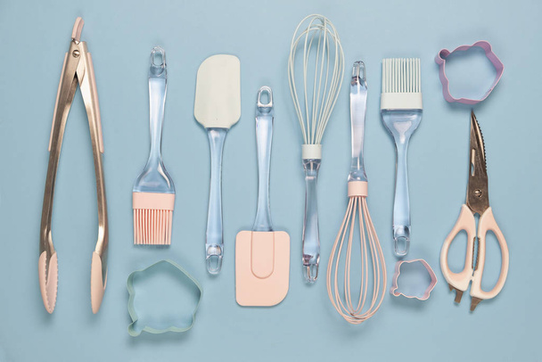 Metal and silicone kitchen utensils in pink color on blue background - Foto, afbeelding