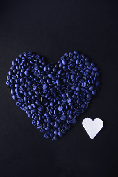 Blue Heart made from coffee beans on a black background with a white clay heart. - Zdjęcie, obraz