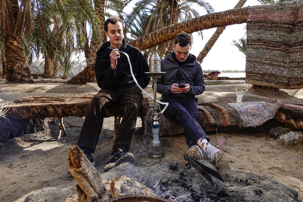 Сіва Оазис, Єгипет Двоє чоловіків курять трубку шиші біля багаття. - Фото, зображення