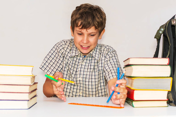 Cheerful teen boy sits at a table with books and does homework - Photo, Image