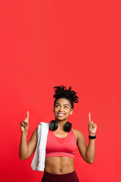 fröhliches afro sportliches Mädchen mit Handtuch und Kopfhörern, die nach oben zeigen - Foto, Bild