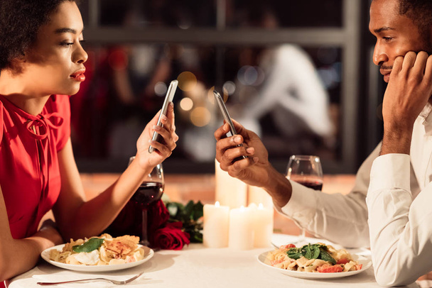 Coppia afroamericana annoiata che utilizza i telefoni durante la data nel ristorante
 - Foto, immagini