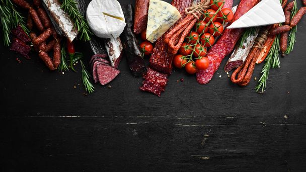 Assortment of cheese, salami, sausage, spices and meat products, on black background. Top view. Free space for your text. - Photo, image