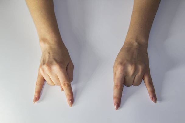 Složení ženských rukou, které ukazují vzhůru nohama rock roll znamení na světlém pozadí. Ženský ruce a nápis rock roll. Koncept s ženskými rukami. - Fotografie, Obrázek