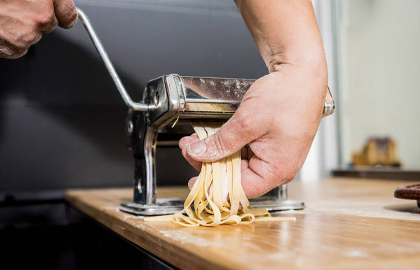 Chef rolling dough with a pasta machine. Pasta maker machine. Homemade italian style cuisine. Restaurant. - 写真・画像