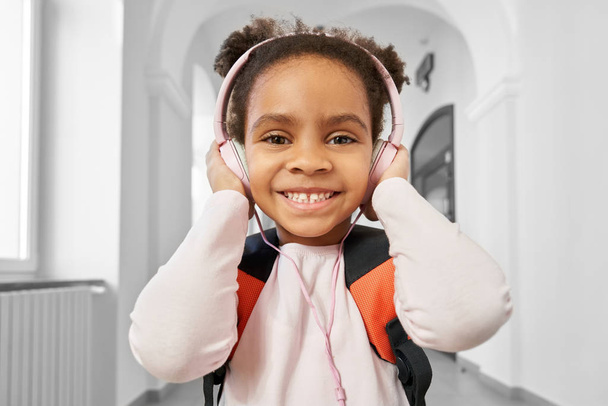 Positief Afrikaans meisje draagt grote roze koptelefoon. - Foto, afbeelding