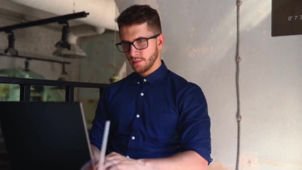 Young attractive hipster freelancer working remotely on laptop in loft cafe. Businessman browsing internet at coffeshop. Blogger posts to social media on travel using 5g internet. Telecommuting theme. - Кадри, відео