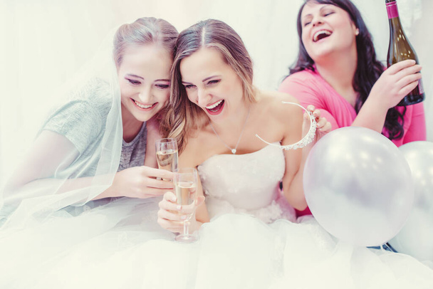 Невеста и подружки невесты веселятся и пьют, покупая свадебное платье
 - Фото, изображение