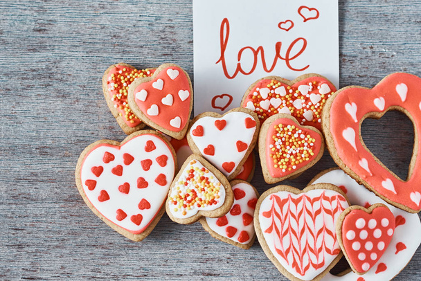 Zdobené a glazované sušenky ve tvaru srdce a papírová poznámka s nápisem Láska na šedém pozadí, pohled shora. Valentines day concept - Fotografie, Obrázek