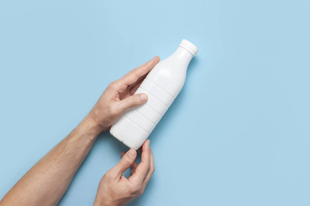 Recipientes de garrafa de plástico branco para produtos lácteos em mãos masculinas sobre fundo azul vista superior flat lay. Garrafa de leite de iogurte Kefir plástico. Modelo de embalagem mockup. Layout para o seu design
 - Foto, Imagem
