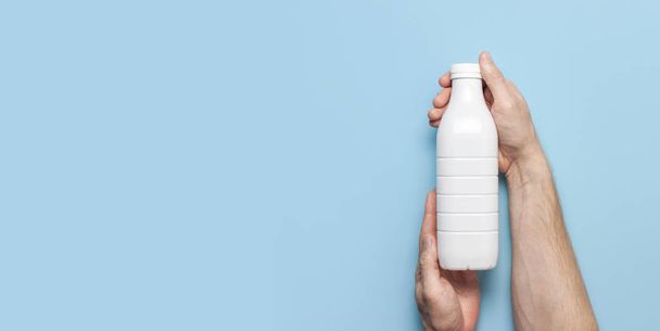 Recipientes de garrafa de plástico branco para produtos lácteos em mãos masculinas sobre fundo azul vista superior flat lay. Garrafa de leite de iogurte Kefir plástico. Modelo de embalagem mockup. Layout para o seu design
 - Foto, Imagem