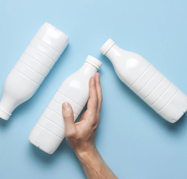 青い背景に男性の手の乳製品のための白いプラスチックボトル容器フラットレイアウトを表示します。プラスチックケフィアヨーグルトミルクボトル。パッケージテンプレートのモックアップ。デザインのレイアウト - 写真・画像
