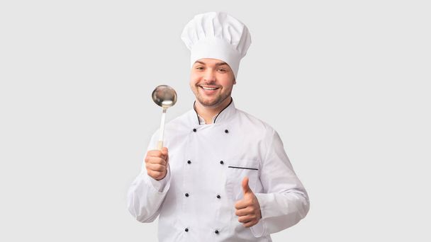 Chef-kok Man Holding Ladle Gesturing Duimen-Up Staande Over Witte Achtergrond - Foto, afbeelding