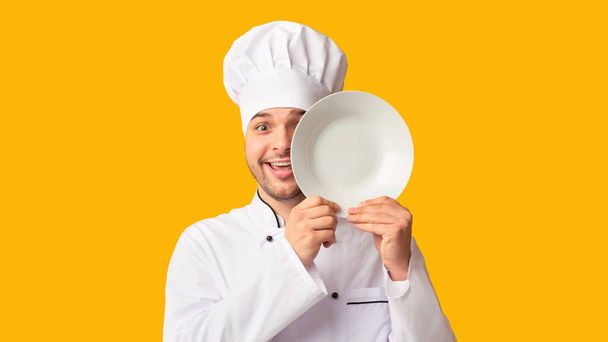 lustige Koch Mann bedeckt Auge mit Teller über gelbem Hintergrund - Foto, Bild