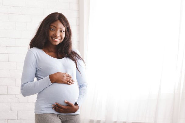 Hymyilevä raskaana afro nainen poseeraa kotona
 - Valokuva, kuva