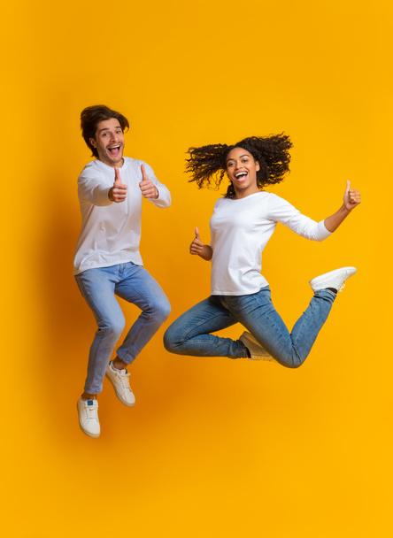 Emocionada pareja multirracial saltando y gestos pulgares hacia arriba, divirtiéndose juntos
 - Foto, imagen