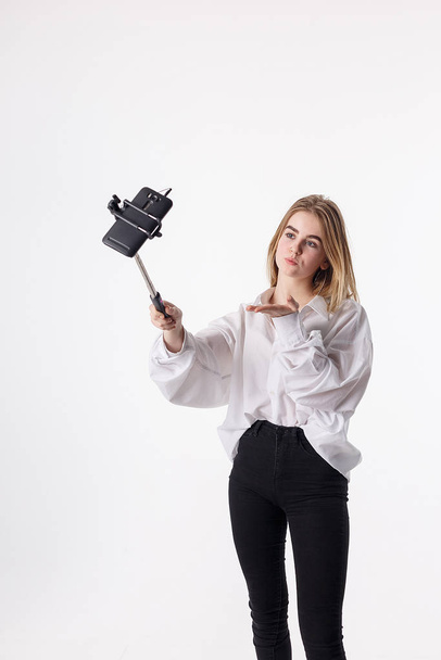 young pretty girl making self portrait with smartphone attached to selfie stick - Photo, image