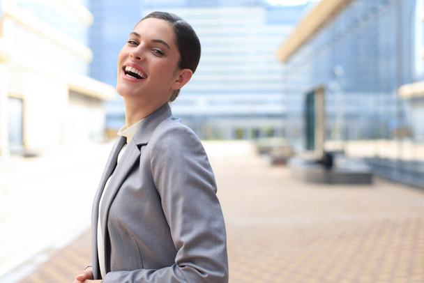 Attractive young woman in suit looking at camera and smiling while standing outdoors. - 写真・画像