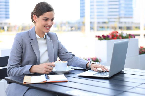 Portrait of successful business woman using laptop and smiling while sitting in cafe, outdoor. - 写真・画像