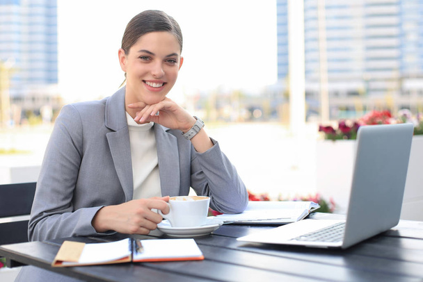 Portrait of successful business woman using laptop and smiling while sitting in cafe, outdoor. - Foto, Bild