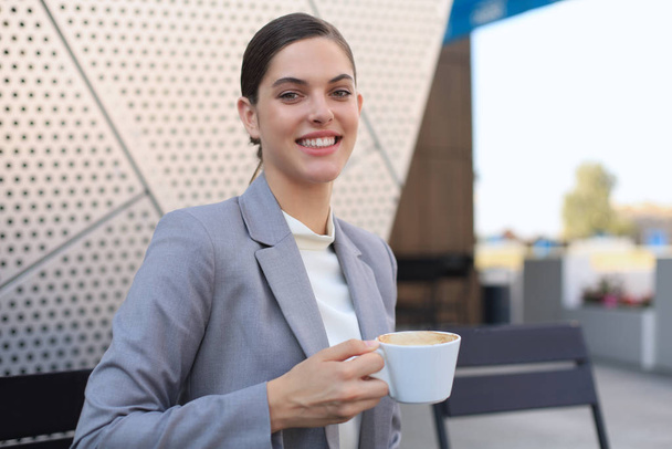 Atrakcyjny uśmiechnięty bizneswoman siedzi w kawiarni z filiżanką kawy. - Zdjęcie, obraz