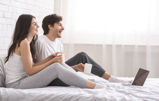 Gli sposi felici che guardano il video sul computer portatile e ridono a letto
 - Foto, immagini