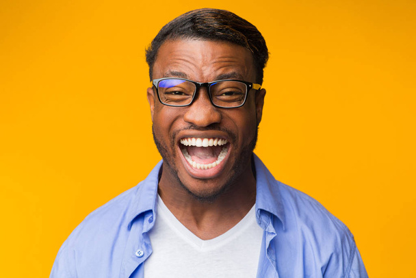 Millennial zwarte man lachen kijkend naar camera over gele achtergrond - Foto, afbeelding