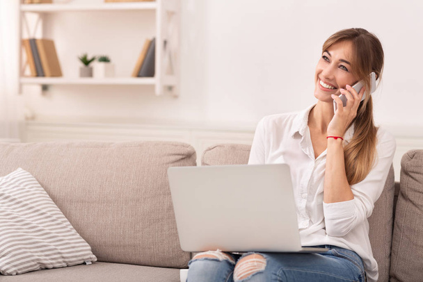 Cheerful Girl Talking On Phone Sitting With Laptop Indoor - Photo, Image