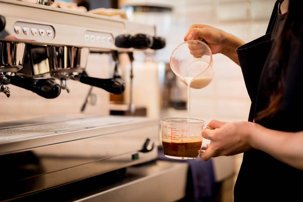 Woman barista pours milk into coffee making iced coffee. - 写真・画像