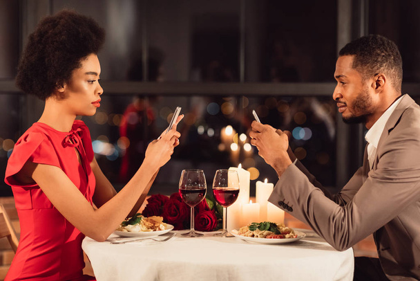 Couple afro-américain utilisant des téléphones mobiles ayant rendez-vous au restaurant
 - Photo, image
