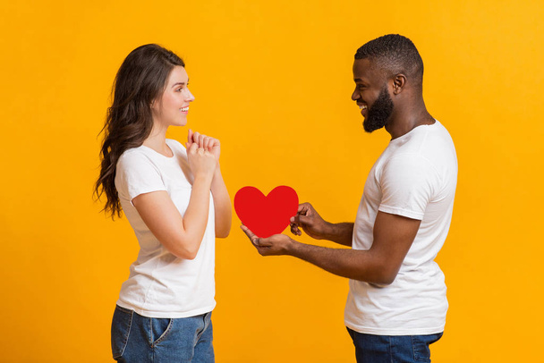 Romantik Siyah Erkek Arkadaşı Şaşırmış Kız Arkadaşına Kırmızı Kağıt Kalp Sunuyor - Fotoğraf, Görsel