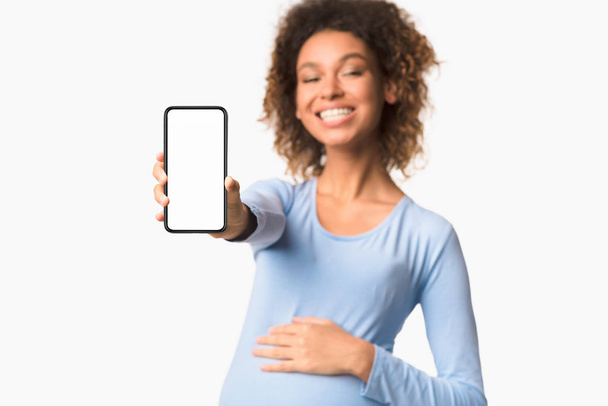 Zwangerschapstoepassingen. Afro dame toont mobiele telefoon met leeg scherm - Foto, afbeelding