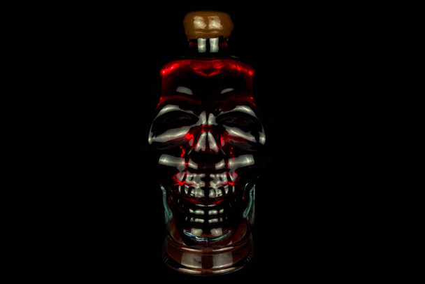стеклянная закрытая бутылка в форме черепа со спиртом внутри, светится красным на черном фоне
 - Фото, изображение