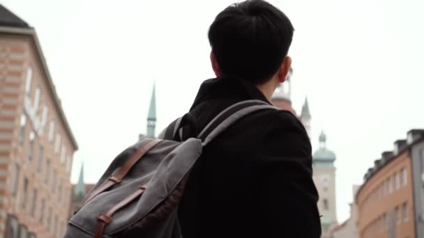 Young Asian man tourist traveling in city centre in Europe. Male backpacker walking in Marienplatz square, Munich, Germany - Filmagem, Vídeo