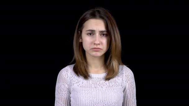 Egy fiatal nő szomorúságot mutat az arcán. A nő szomorú egy fekete háttér. - Felvétel, videó