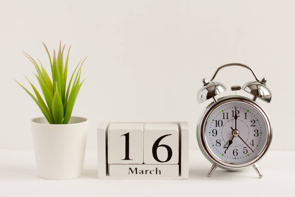 March 16 on a wooden calendar next to an alarm clock and a flower on a white background. The concept of one day a year.Significant date or event - Foto, Bild
