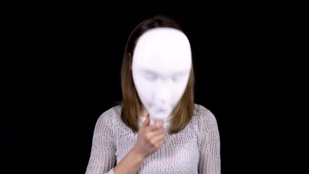 Une jeune femme enlève le masque et montre de la tristesse sur son visage. La fille regarde tristement la caméra. Femme cache son visage derrière un masque blanc sur un fond noir
. - Séquence, vidéo
