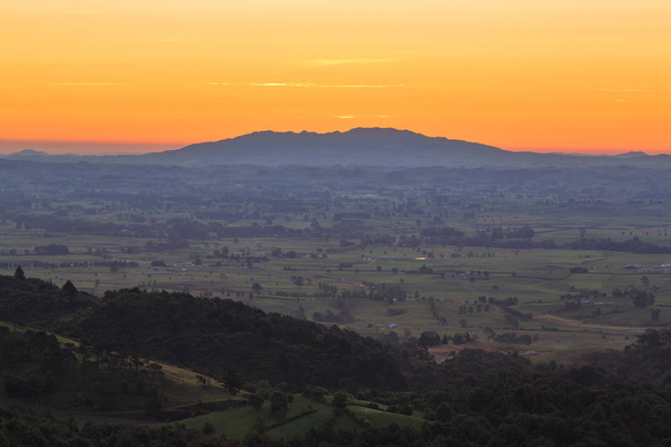 Zemědělská země regionu Waikato, Nový Zéland, spatřena při západu slunce z pohoří Kaimai. Na obzoru je Maungatautari, nebo Santuary Mountain, útočiště divoké zvěře - Fotografie, Obrázek