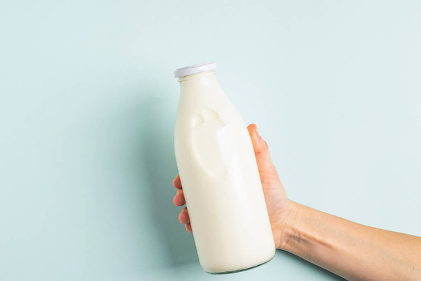 Female hand holds milk or white milk drink in a glass bottle on white background. Healthy eating concept. Flat layout . - Фото, зображення