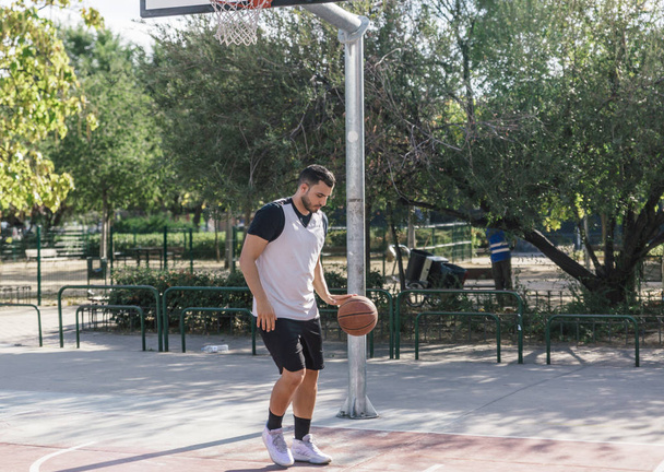 Atletik tenli oyuncu açık hava sahasının ortasında basketbol oynuyor. - Fotoğraf, Görsel