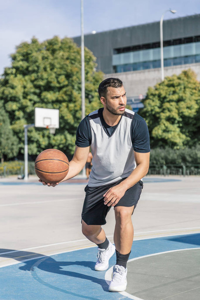 Koszykarz niesie w prawej ręce koszykówkę podczas gry na boisku zewnętrznym - Zdjęcie, obraz