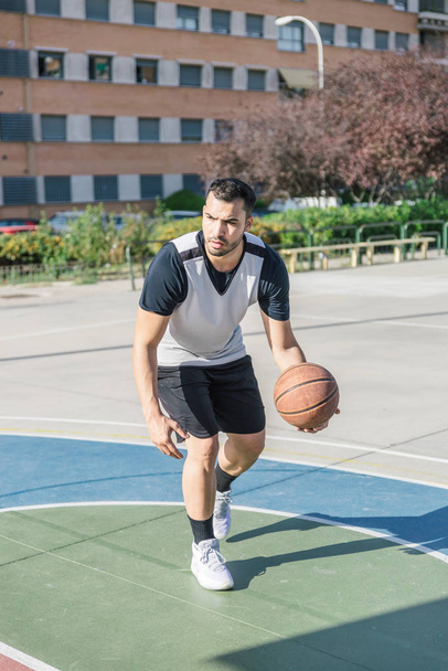 Basketbolcu şehir basketbol sahasında oynarken sol koluyla topunu oynatıyor. - Fotoğraf, Görsel