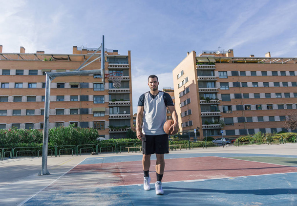 Full body view van een sterke urban basketbalspeler op een buitenbaan - Foto, afbeelding