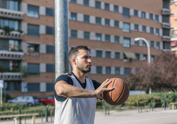 Сильный баскетболист опирается на металлическую колонну своим мячом
 - Фото, изображение