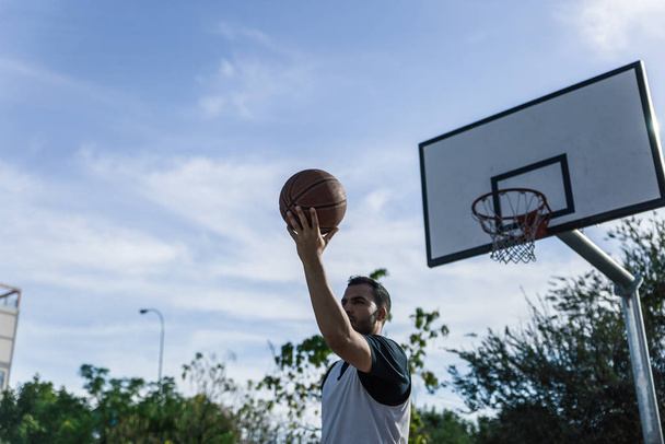 Basketball player throws the ball with his back to the basket of an outdoor court - Φωτογραφία, εικόνα