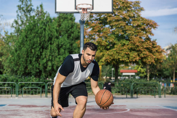 Urban Athlet übt Basketball auf einem Außenplatz und spielt mit dem Ball mit dem linken Arm - Foto, Bild