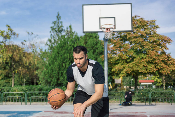 Genç oyuncu sahanın dışında basketbol antrenmanı yapıyor. Sağ koluyla top oynuyor. - Fotoğraf, Görsel