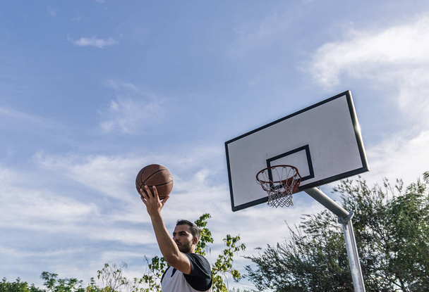Basketball player throws the ball with his back to the basket of an outdoor court - Foto, Bild