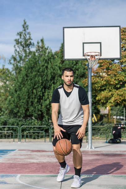 Junger Spieler übt Basketball auf einem Außenplatz und spielt mit dem Ball mit dem rechten Arm - Foto, Bild